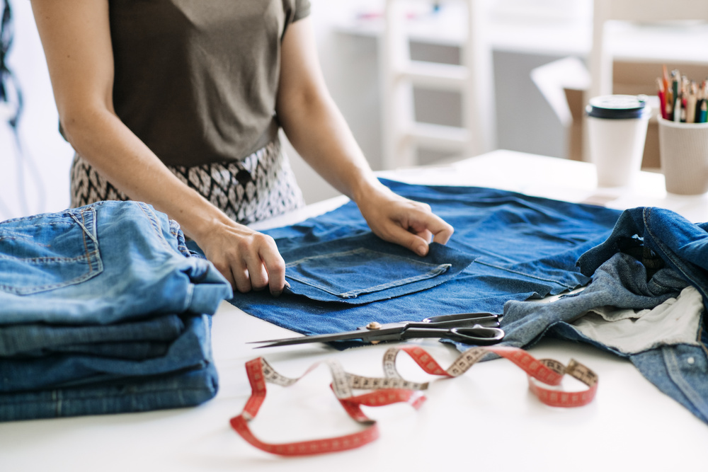Circular Economy. Sustainable Fashion. Reuse, Repair, Upcycle. Denim Upcycling Ideas, Repair and Using Old Jeans. Woman Seamstress Repair Old Denim Jeans in Sewing Studio.